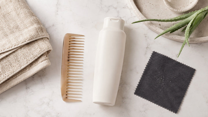 Gentle scalp-care still life with comb, shampoo, towel, aloe, and visible flakes